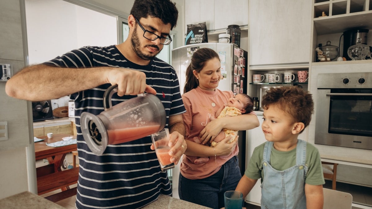 a man pours a drink for two children in a kitchen